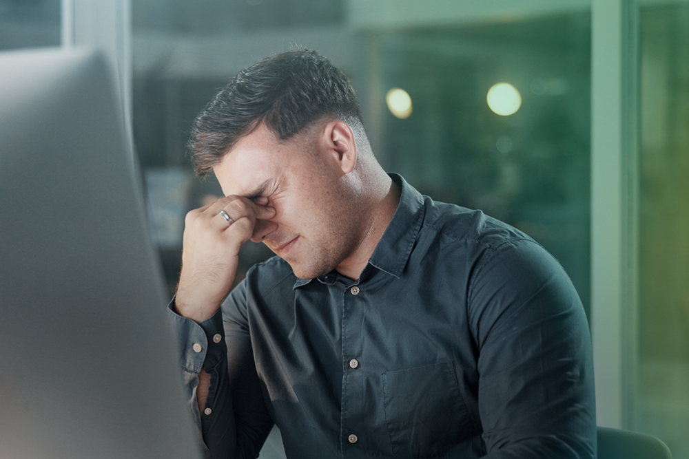 Business professional experiencing stress while working at a computer due to payroll challenges.